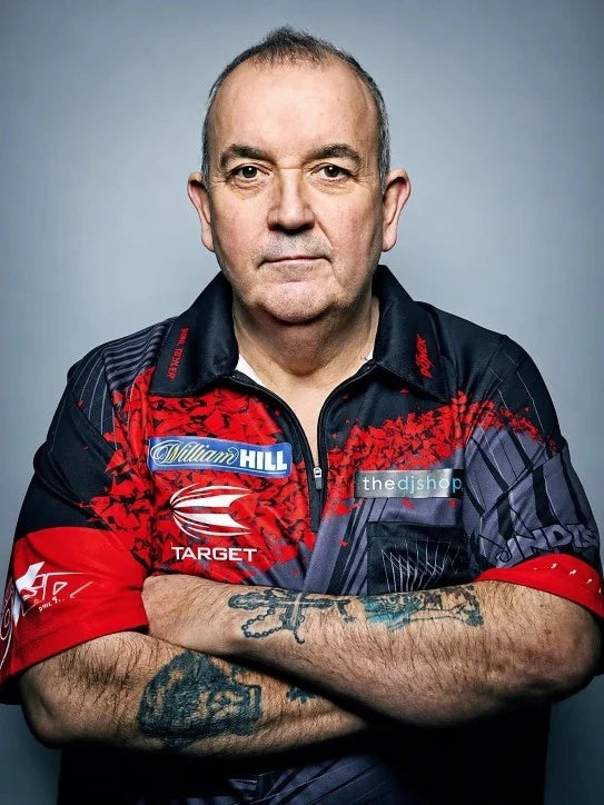 Phil Taylor in een rood-zwart dartshirt met sponsorlogo’s en gekruiste armen.