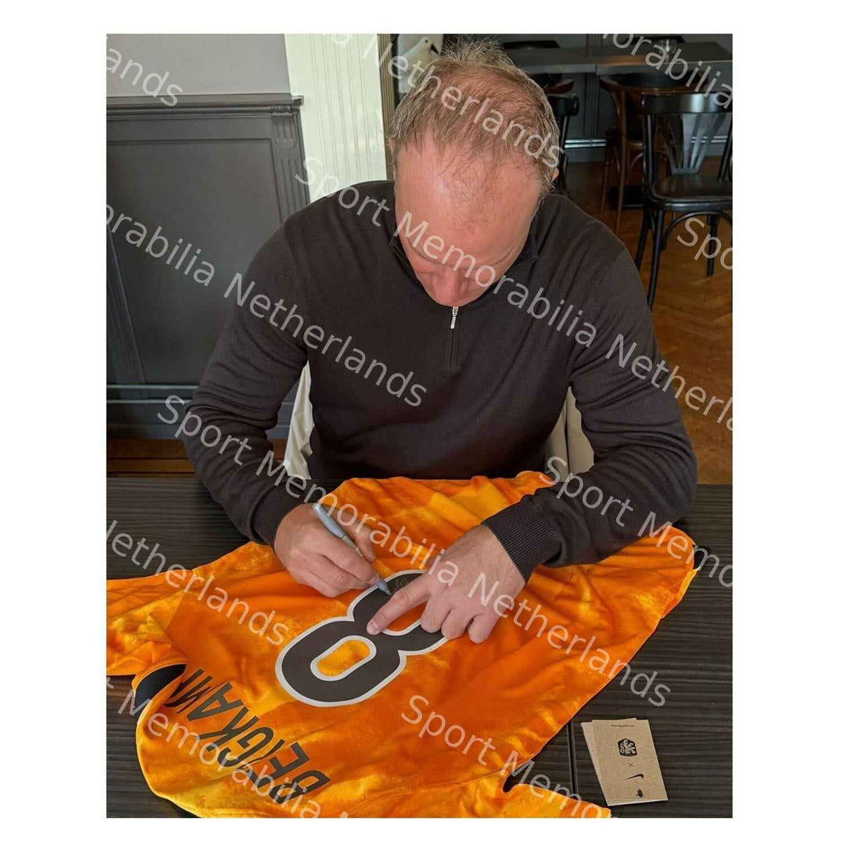 Dennis Bergkamp tijdens het signeren van een oranje Nederland nummer 8 voetbalshirt.
