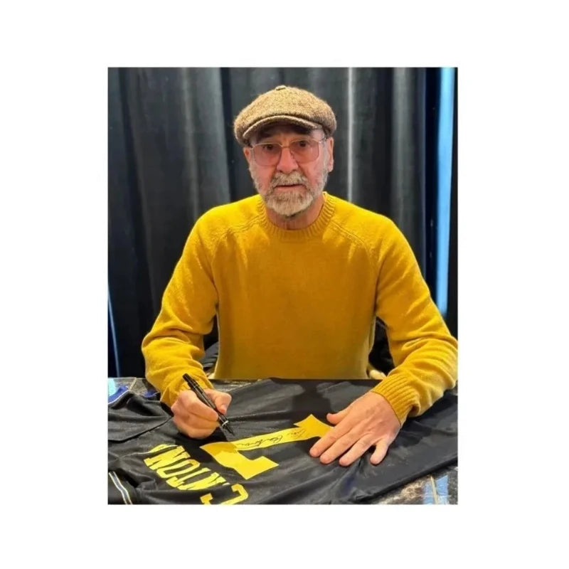 Eric Cantona signeert een zwart Manchester United 1994-1996 replica uitshirt tijdens een signeersessie op 2 december 2025 in Parijs, als fotografisch bewijs van de handtekening.