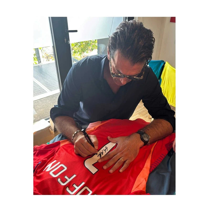 Gianluigi Buffon signeert een rood Juventus keepersshirt met rugnummer 1 tijdens een signeersessie. De handtekening wordt op het witte rugnummer geplaatst.