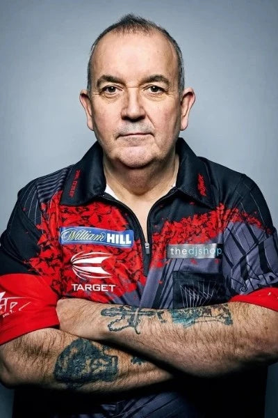 Phil Taylor in een rood-zwart dartshirt met sponsorlogo’s en gekruiste armen.