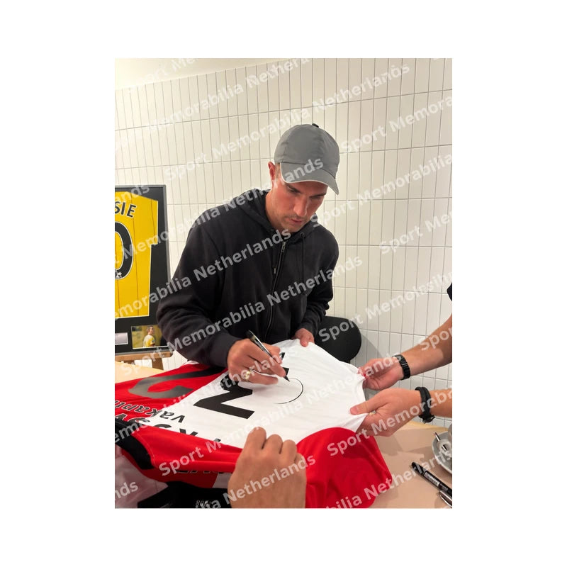 Robin van Persie signeert een rood-wit Feyenoord voetbalshirt tijdens een signeersessie. Signing proof met zichtbaar handtekeningmoment en watermerk van Sport Memorabilia Netherlands.