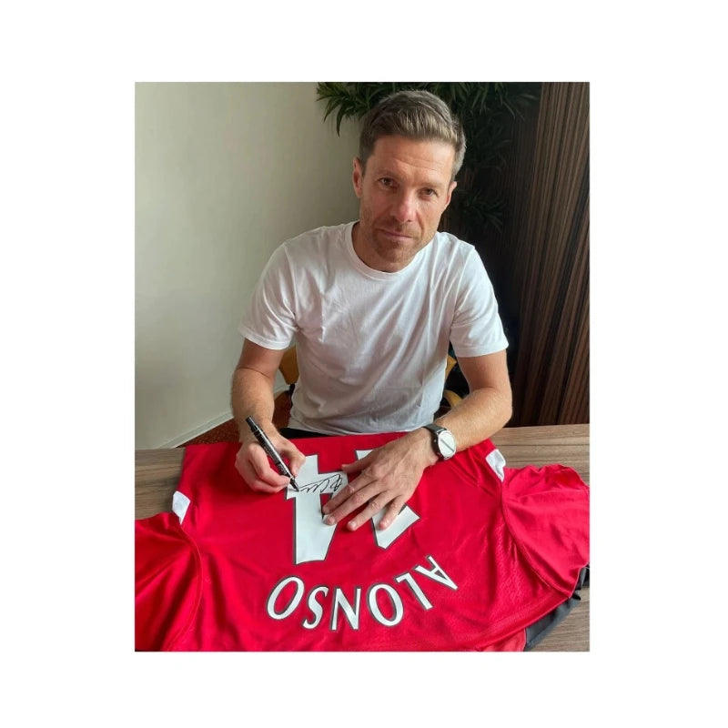Xabi Alonso signeert een rood Liverpool 2005 replica voetbalshirt op het witte rugnummer 14 tijdens een signeersessie op 13 augustus 2024 in Leverkusen.